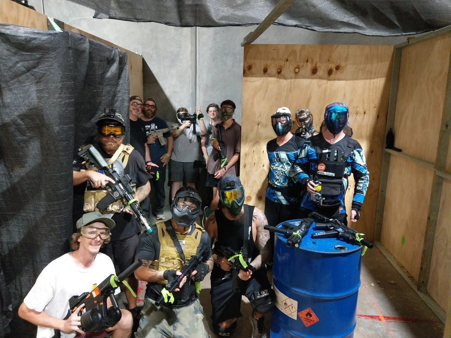 A group of gel ball players in masks and jerseys with gel blasters gathered by a gel-splattered barrel in the indoor CQB arena at Urban Gel Ball, Queensland